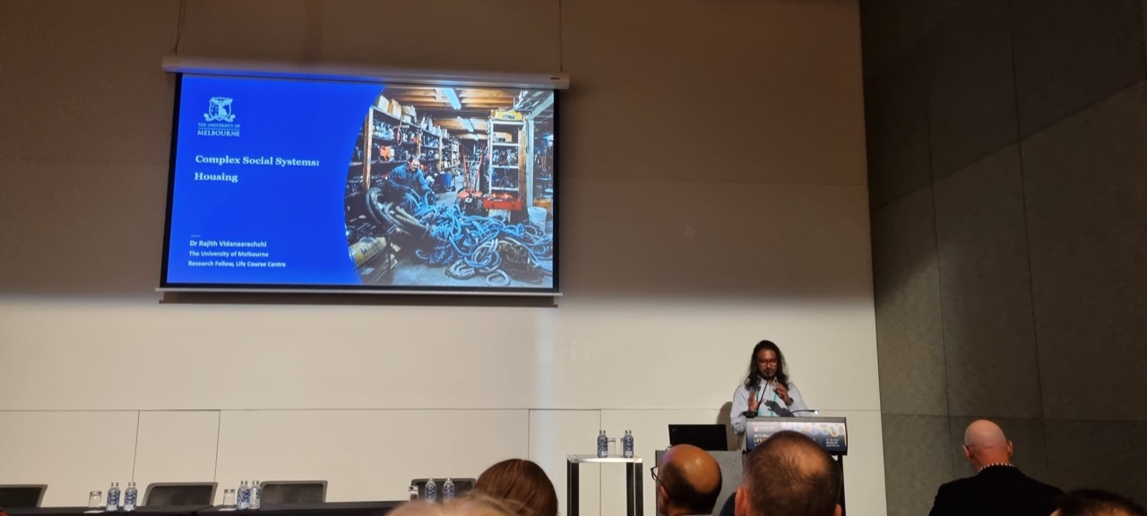 Rajith Vidanaarachchi presenting 'Complex Social Systems: Housing' at a podium at the International Life Course Conference 2025